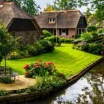 Scenic canal in Giethoorn village featuring traditional thatched roof houses and wooden footbridges in summer