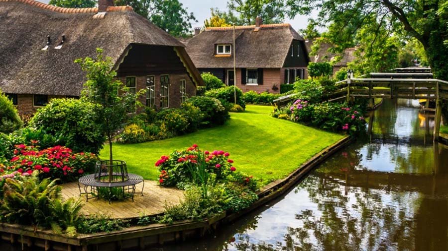 Scenic canal in Giethoorn village featuring traditional thatched roof houses and wooden footbridges in summer