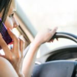 Close-up of a driver holding a smartphone while steering, illustrating the dangers of distracted driving