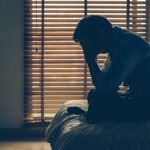 A stressed person sitting on the edge of a bed at night suffering from insomnia and sleep anxiety.