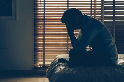 A stressed person sitting on the edge of a bed at night suffering from insomnia and sleep anxiety.