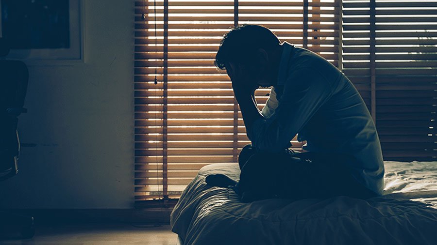 A stressed person sitting on the edge of a bed at night suffering from insomnia and sleep anxiety.