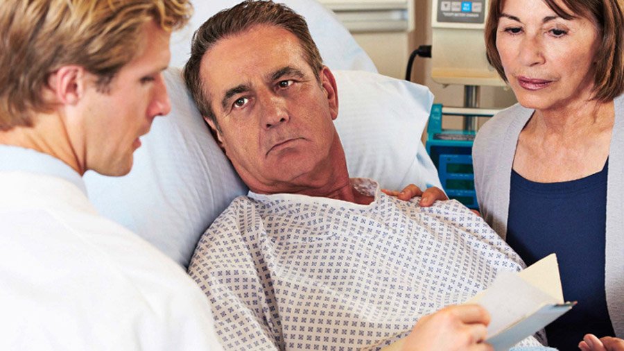 A doctor and a patient's wife engaging in a focused and respectful discussion at his bedside in a hospital
